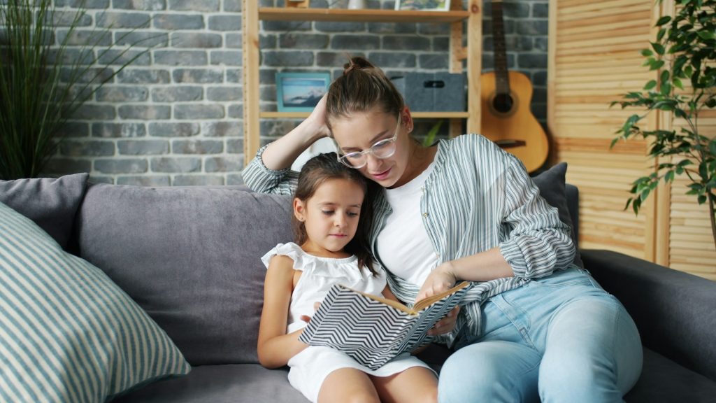 madre e hija leyendo un cuento juntas en el sofá
